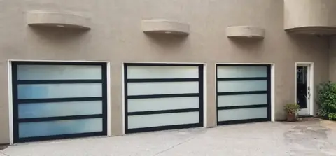 Three full-view garage doors with black frames and white laminated glass in wide horizontal lites, set in a beige stucco wall