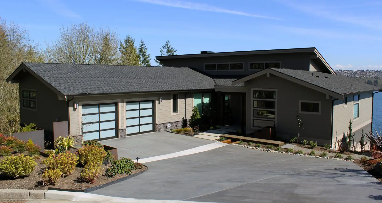 Two single full-view garage doors, 2 lites by 4, with dark bronze frames and white laminated glass on a gray lap-sided house