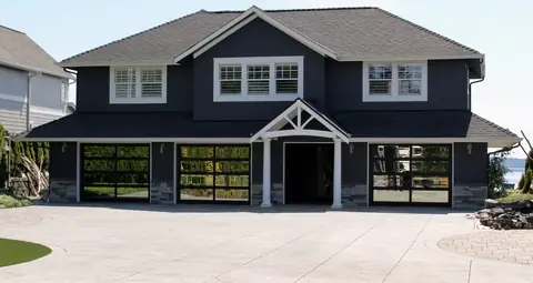 Three single full-view garage doors, 2 lites by 4, with black frames and mirror glass on a navy house with a portico