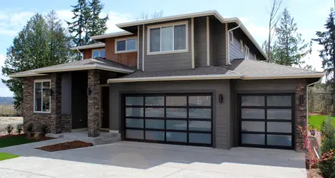 A double and a single full-view garage door with black frames and satin etched glass on a gray lap-sided house