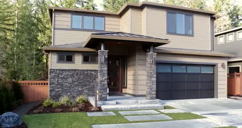 Double garage door in dark bronze aluminum with solid panels and one row of glass across the top, on a tan house
