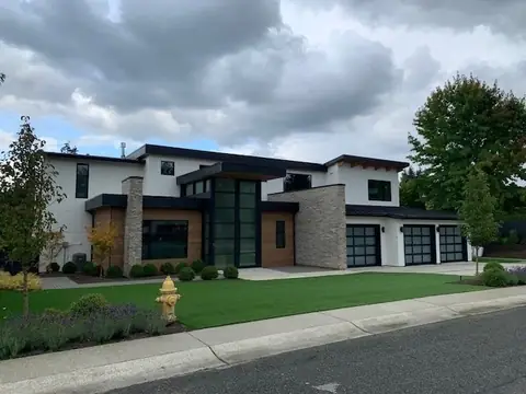 Three single full-view garage doors with black frames and dark glass at the end of a large white stucco modern house