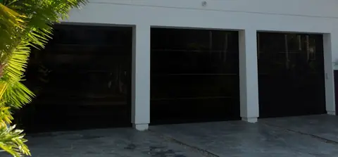 Three single frameless full-view garage doors in glossy black glass, set between square white piers on a white wall