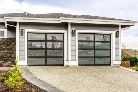 Two single full-view aluminum garage doors with dark frames and satin glass reflecting trees, on a gray sided house.