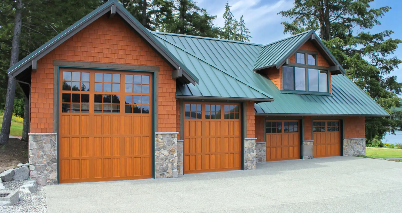 Four wood-look carriage garage doors with divided-lite windows, one extra tall, on a cedar shingle shop with a green metal roof.
