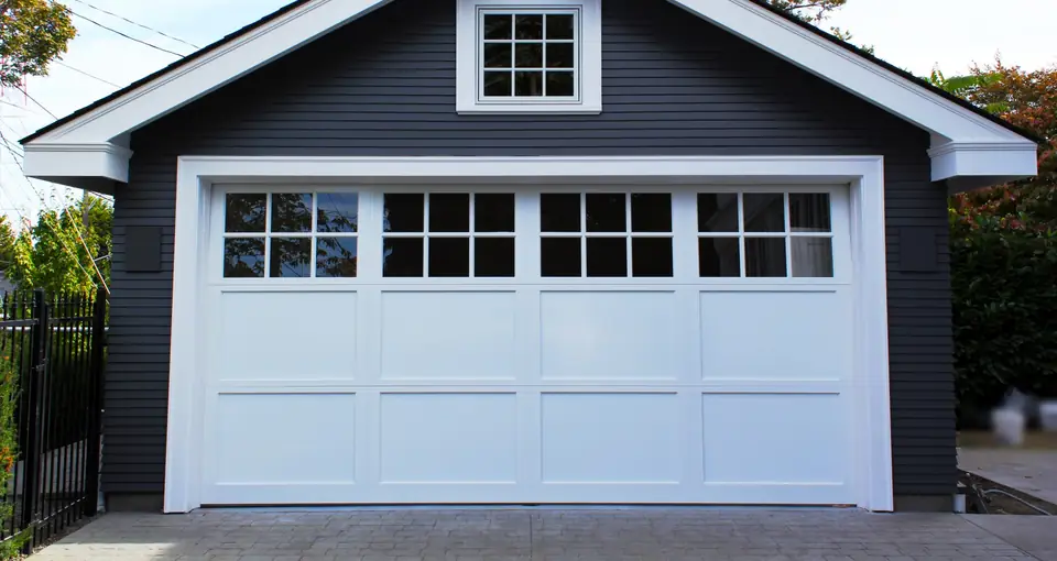 White double carriage-style garage door with a top row of divided-lite windows over flat panels, on a charcoal sided garage.