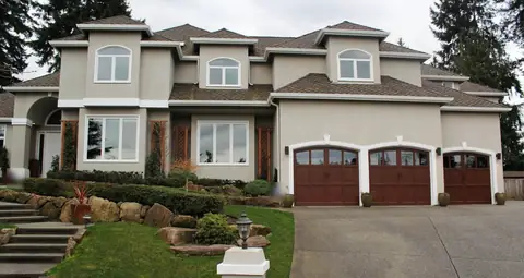 Three single arched-top carriage garage doors in a mahogany wood-look finish with top windows, on a gray stucco house.
