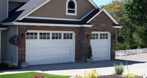 White double and single garage doors with small recessed panels and divided-lite top rows, set in red brick.
