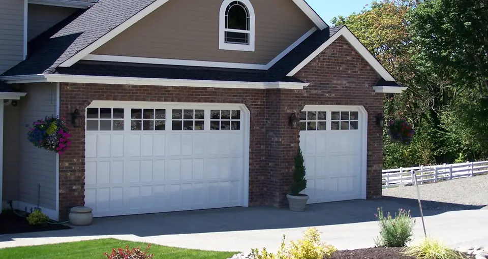 White double and single garage doors with small recessed panels and divided-lite top rows, set in red brick.
