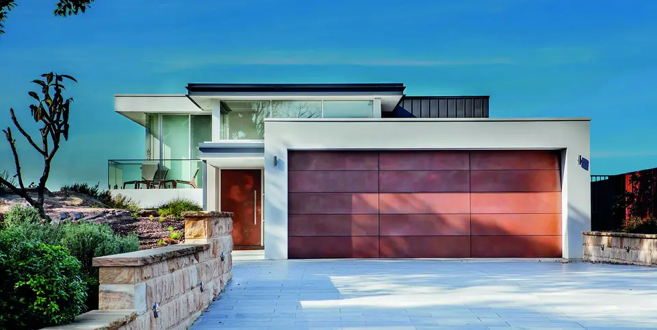 Double garage door in large flush panels with a copper metal finish, beside a matching front door on a white house.