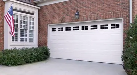 White short-panel steel double garage door with a top row of small black-gridded windows, set in a red brick wall