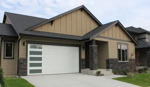 White steel garage door with faint horizontal grooves and five frosted windows down the left side, on a tan lap-sided house