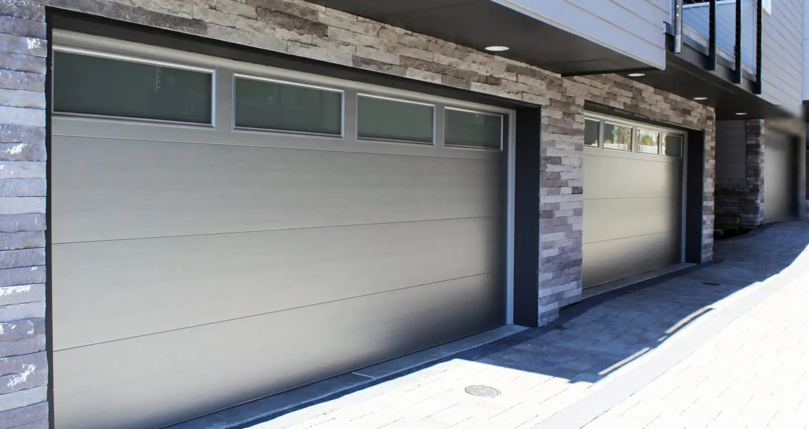 Brushed silver flush steel garage doors with a top row of four frosted windows, in a row of stacked-stone townhouse garages