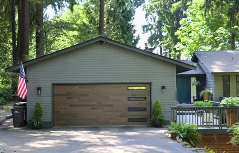 Double garage door in mixed brown wood-look planks with four slim windows stacked at the right, on a green lap-sided gable garage