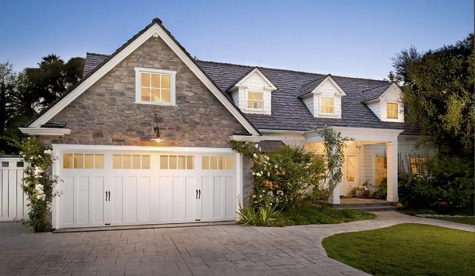 White carriage-house double garage door with square top windows and black handles, set in a stone gable of a house with dormers
