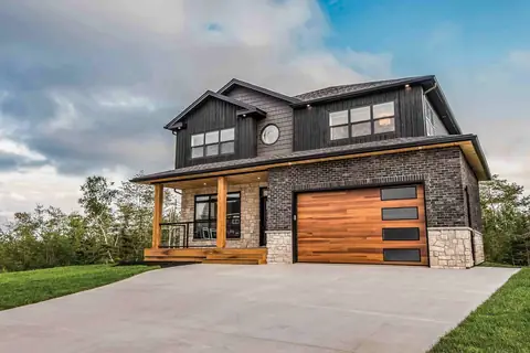 Single garage door of horizontal cedar-toned planks with four dark glass windows in black frames stacked on the right, in a dark brick two-story house.