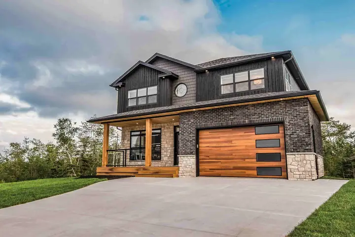 Single garage door of horizontal cedar-toned planks with four dark glass windows in black frames stacked on the right, in a dark brick two-story house.