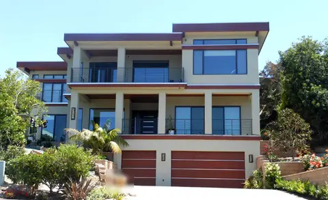 Single and double mahogany-stained flush wood garage doors with thin light metal strips across them, at the base of a three-story stucco house.