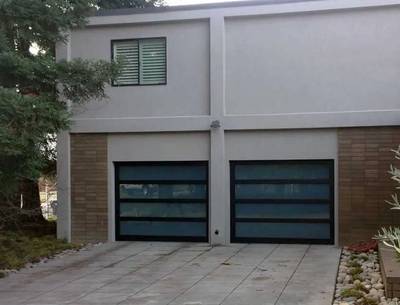 Two full-view black-framed garage doors with frosted glass under a gray stucco house