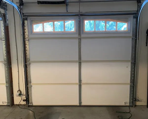 Inside a garage: a white sectional door with arched window lites, closed, seen from behind, with its tracks at each side