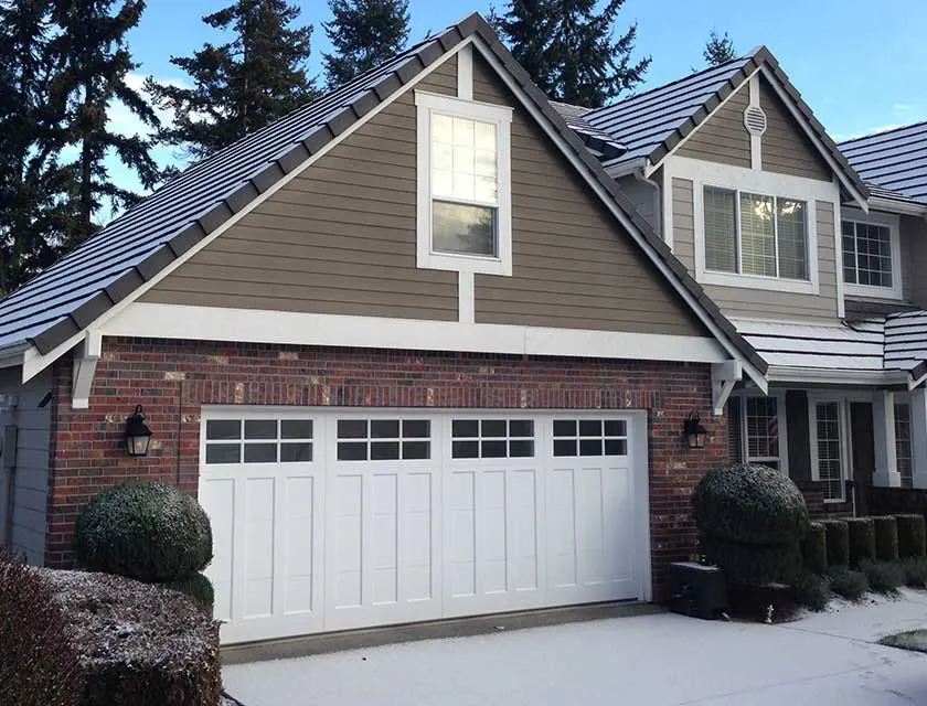 A white garage door with a row of lights across the top, under a steep gable on a brick house